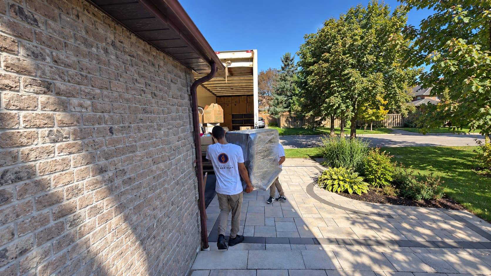 Movers carrying furniture along the side of a brick house to the moving truck